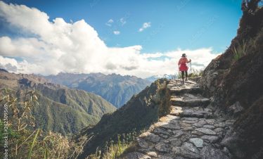 A female hiker is walking on the famous Inca trail of Peru with walking sticks. She is on the way to Machu Picchu.