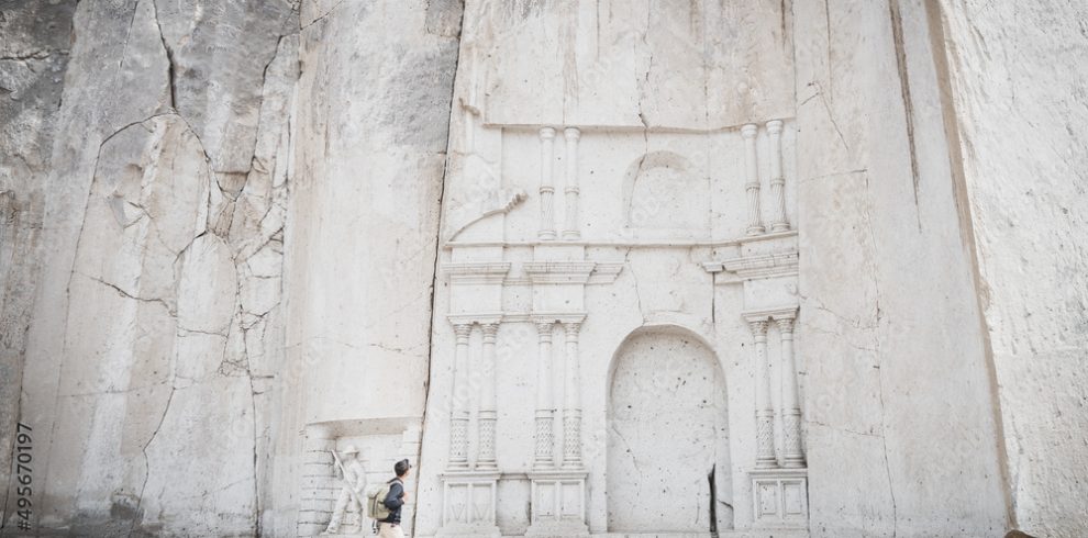 Wide angle view of a caucasian man looking at the stone wall sculpture of Petra in Ruta del Sillar, Arequipa, Peru.